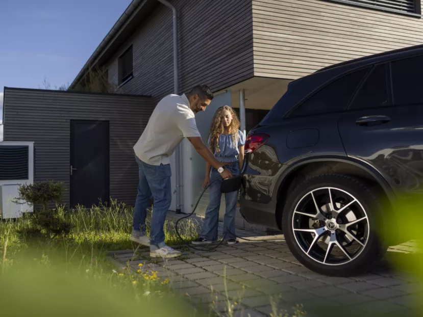 Haus der Energie – Elektroauto zuhause laden Mann und Kind laden ein Elektroauto vor ihrem Haus – im Kontext von Haus der Energie