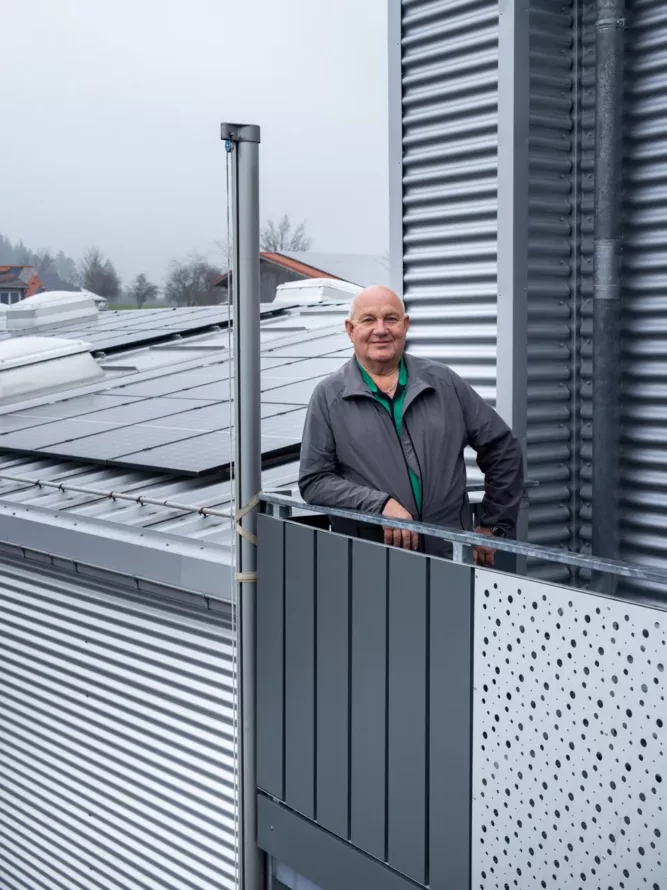 Haus der Energie – Photovoltaik auf Mehrfamilienhaus Mann steht auf einem Balkon eines Gebäudes mit Photovoltaikanlage von Haus der Energie auf dem Dach