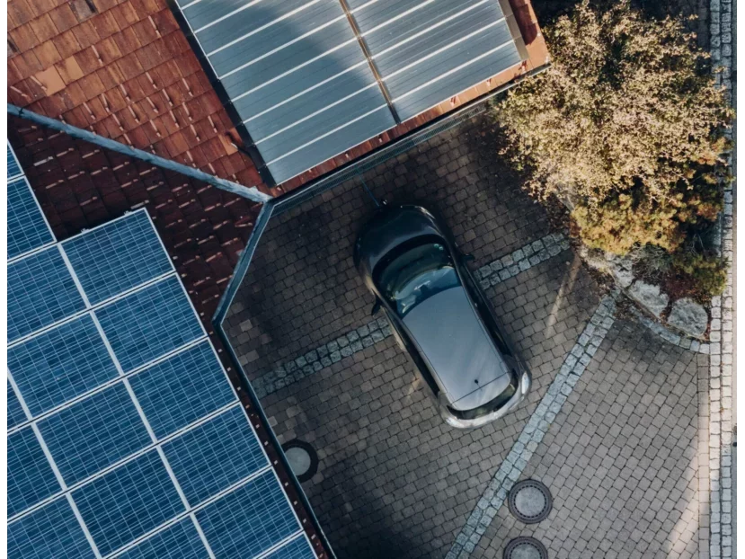 E-Mobilität: Luftaufnahme eines Hauses als Haus der Energie mit Energiesystemen auf dem Dach und einem Auto in der Einfahrt
