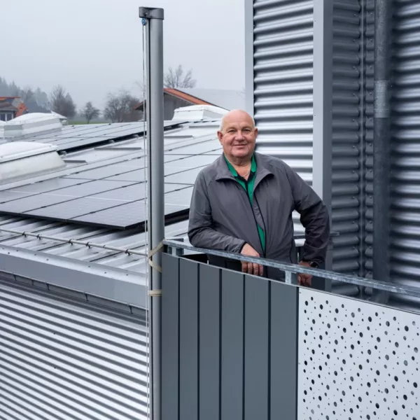 Mann steht auf einem Balkon eines Gebäudes mit Photovoltaikanlage von Haus der Energie auf dem Dach