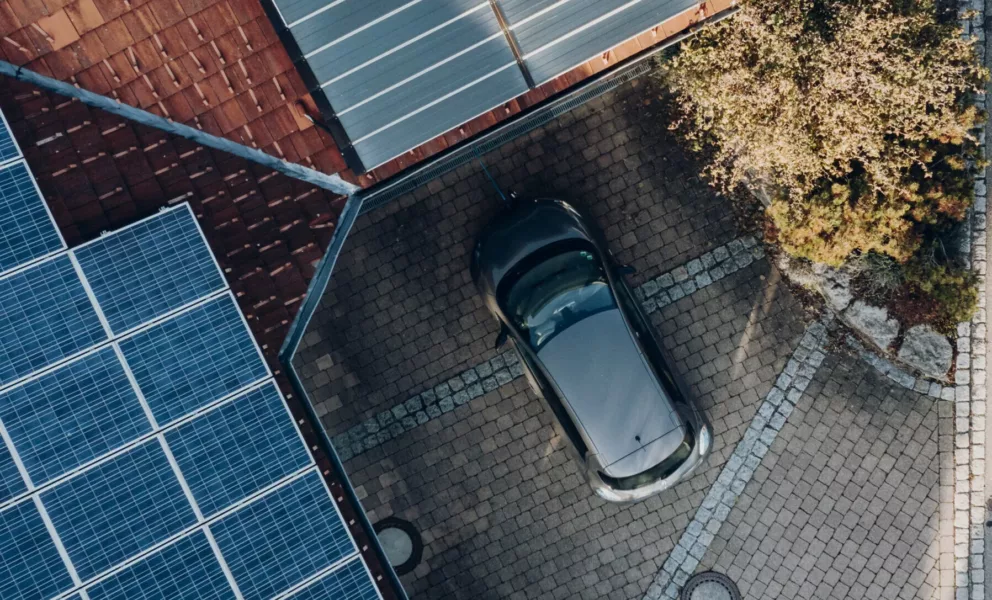 E-Mobilität: Luftaufnahme eines Hauses als Haus der Energie mit Energiesystemen auf dem Dach und einem Auto in der Einfahrt